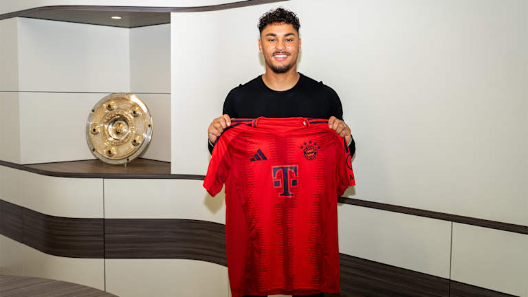 Armindo Sieb hält nach der Vertragsunterschrift ein Trikot des FC Bayern hoch.