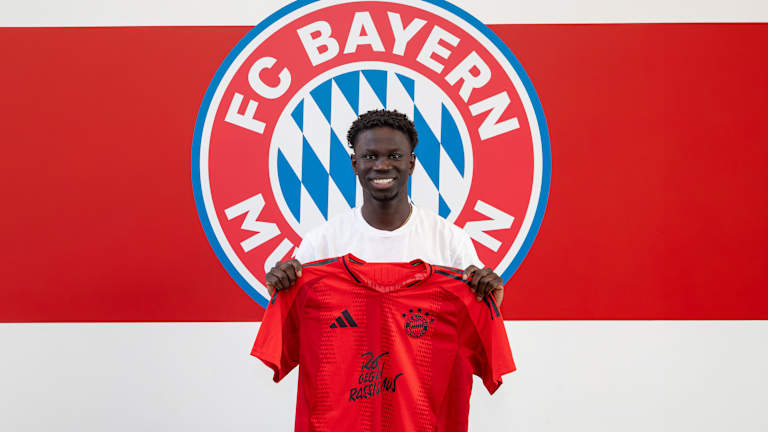 Bajung Darboe, FC Bayern Amateure-Neuzugang, hält ein FC Bayern Heimtrikot in seinen Händen.