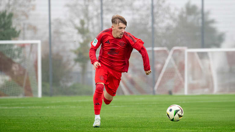 Lennart Karl im Heimtrikot des FC Bayern dribbelt mit dem Ball an seinem Fuß.
