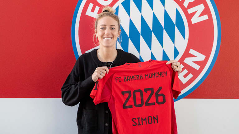 Carolin Simon posiert vor dem FC Bayern Logo mit einem Trikot mit der Rückennummer 2026.