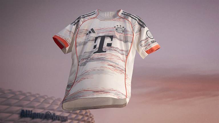 La nueva segunda equipación del FC Bayern para la temporada 2025/26 en blanco, gris y coral brillante ondea frente al Allianz Arena.