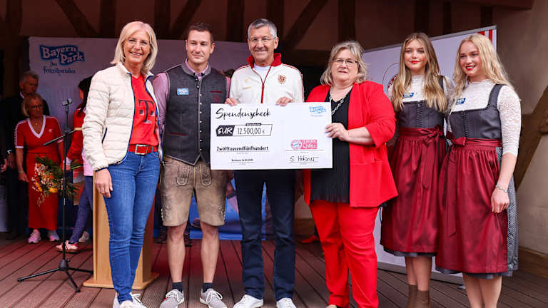 El presidente Herbert Hainer muestra un cheque a la cámara ante un grupo de personas en el festival de aficionados en el Bayern Park.