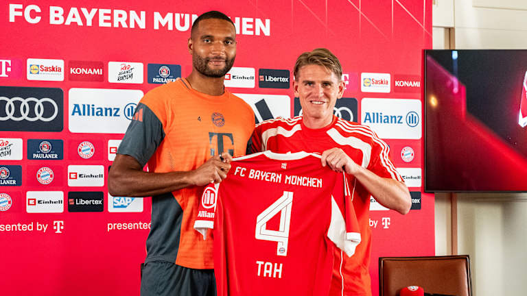 Jonathan Tah und Christoph Freund halten ein FCB-Trikot mit der Rückennummer 4 hoch