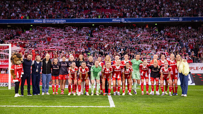Die FC Bayern Frauen in einem Gruppenfoto vor der Südkurve der Allianz Arena mit Fans im Hintergrund.