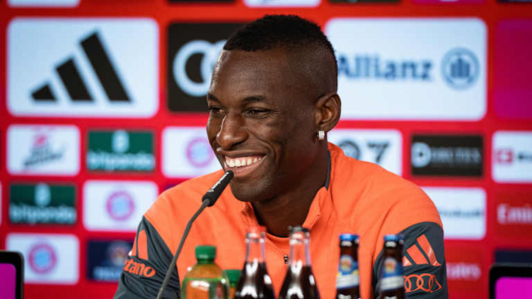 Nicolas Jackson sitzt lachend auf der Medientribüne des FC Bayern