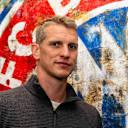 Lars Bender steht vor dem FC Bayern Logo und schaut in die Kamera.
