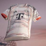 Das neue Auswärtstrikot des FC Bayern für die Saison 2025/26 in Weiß, Grau und leuchtendem Coral schwebt vor der Allianz Arena.