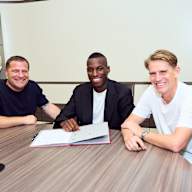 Max Eberl, Nicolas Jackson, Christoph Freund sitzen an einem Tisch, Jackson unterschreibt einen Vertrag