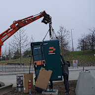 Ein Bagger hebt die  Ladesäule für den E-Ladepark vor der Allianz Arena an