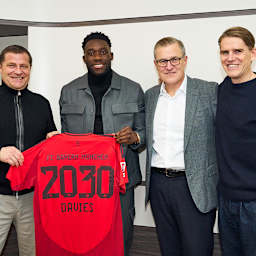 Max Eberl, Alphonso Davies, Jan-Christian Dreesen und Christoph Freund stehen nebeneinander und halten ein Trikot von Alphonso Davies hoch.