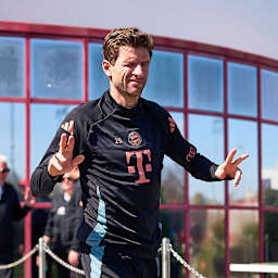 Thomas Müller zwinkert in die Kamera und zeigt das doppelte Victory-Zeichen vor dem Training des FC Bayern