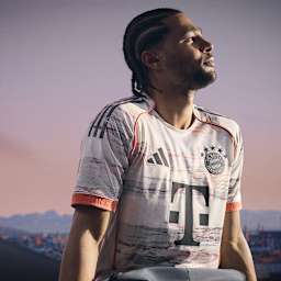 Serge Gnabry im neuen Auswärtstrikot des FC Bayern für die Saison 2025/26 in Weiß, Grau und leuchtendem Coral.