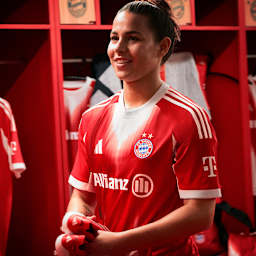 Lena Oberdorf steht in der Kabine und trägt das neue Heimtrikot des FC Bayern in Rot und Weiß mit stilisiertem M.