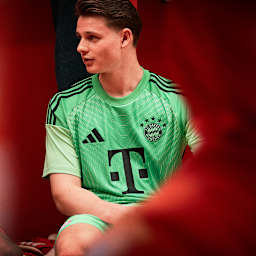 Jonas Urbig sitzt in der Kabine und trägt das neue Torwarttrikot des FC Bayern in Grün.