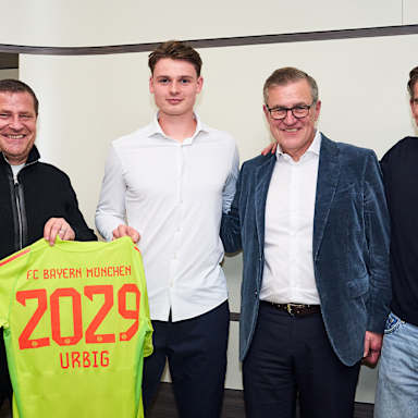 Max Eberl, Jonas Urbig, Jan-Christian Dreesen und Christoph Freund halten ein FC Bayern-Trikot von Urbig mit der 2029 hoch