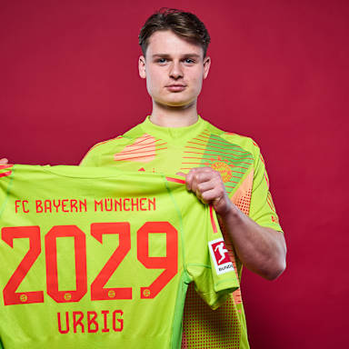 Jonas Urbig hält ein Trikot des FC Bayern mit der Zahl 2029 hoch