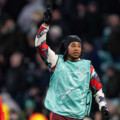 Michael Olise vom FC Bayern deutet beim Aufwärmen im Celtic Park nach oben.