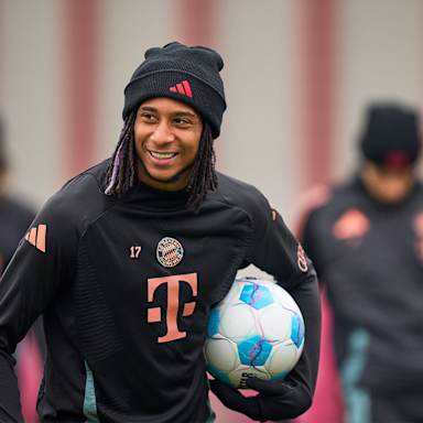 Michael Olise lächelnd mit einem Ball unter dem Arm im FC Bayern-Training vor dem Bundesliga-Spiel bei Union Berlin