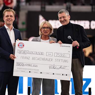 Joel und Heidi Beckenbauer und Herbert Hainer halten einen Scheck beim Beckenbauer Cup hoch.
