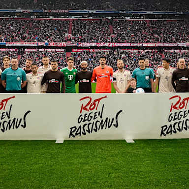 Spieler des FC Bayern und des FC St. Pauli stehen vor dem Spiel hinter einer Bande mit dem Schriftzug Rot gegen Rassismus
