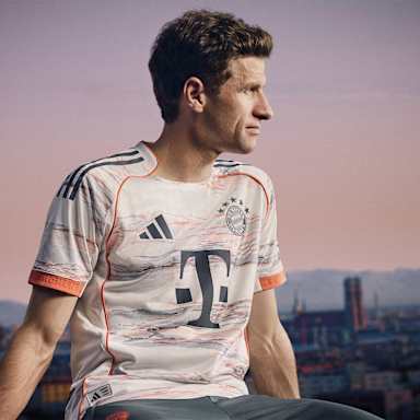 Thomas Müller im neuen Auswärtstrikot des FC Bayern für die Saison 2025/26 in Weiß, Grau und leuchtendem Coral.