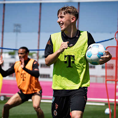 Lennart Karl lachend mit Ball in der Hand im Training des FC Bayern