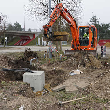 Ein Bagger gräbt ein Loch für die E-Ladesäule am E-Ladepark vor der Allianz Arena