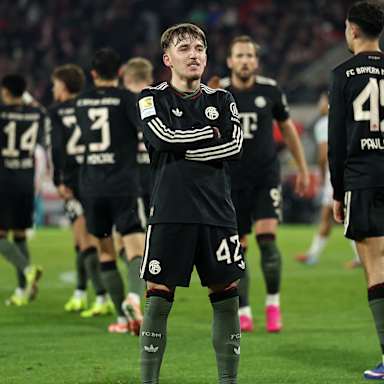 Lennart Karl steht mit verschränkten Armen vor der Kurve nach dem 3:1 im Bundesliga-Spiel des FC Bayern beim 1. FC Köln