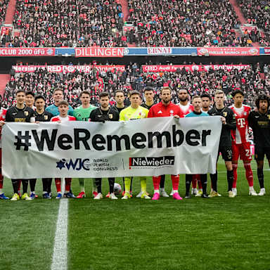 Die Mannschaften des FC Bayern und des FC Augsburg halten vor Anpfiff der Partie ein Banner mit der Aufschrift: #WeRemember