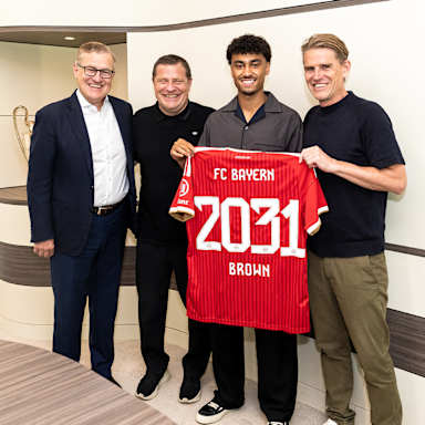 Jan-Christian Dreesen, Max Eberl, Nathaniel Brown und Christoph Freund stehen nebeneinander und halten ein FCB-Trikot mit 2031 Brown