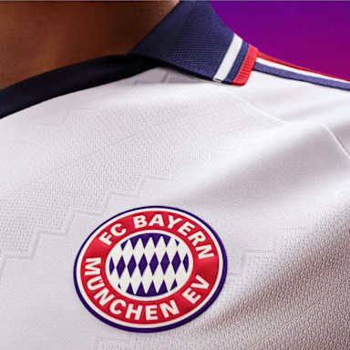 Detailansicht auf das Wappen des FC Bayern auf dem neuen FC Bayern Auswärtstrikot 2026/27 im Retro-Look in schlichtem Weiß mit Polo-Kragen und rot-marineblauen Details