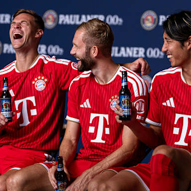 Joshua Kimmich, Konrad Laimer und Hiroki Ito unterhalten sich und lachen im FCB-Trikot mit Paulaner Bier