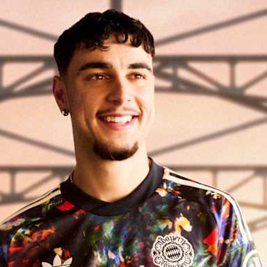 Aleksandar Pavlovic  trägt das neue FC Bayern-Wiesn-Trikot 2026/27 mit farbenfrohem floralen Muster, im Hintergrund ist die Münchner Hackerbrücke zu sehen