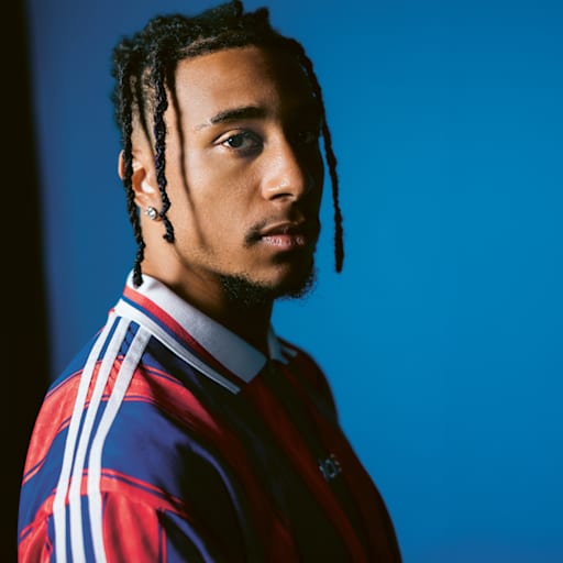 Michael Olise trägt ein FC Bayern-Trikot aus den Neunzigern mit rot-blauen Längsstreifen