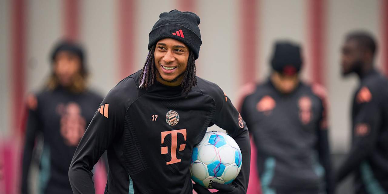 Michael Olise lächelnd mit einem Ball unter dem Arm im FC Bayern-Training vor dem Bundesliga-Spiel bei Union Berlin