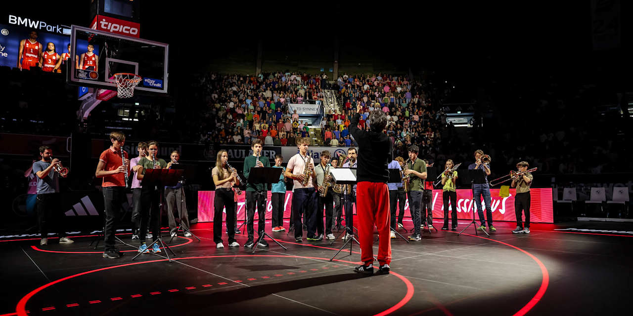 A youth orchestra plays on the basketball court, while the youth choir sings on the stands behind them.