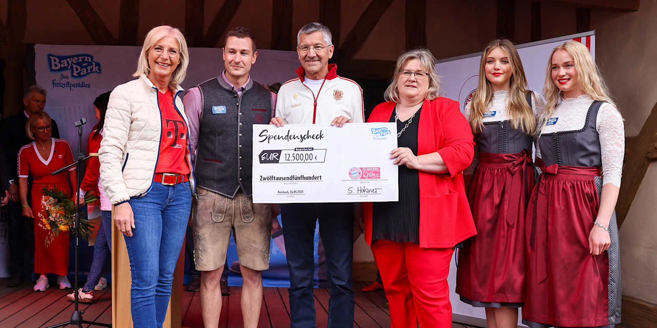 President Herbert Hainer holds up a cheque in a group photo at the fan festival at Bayern Park