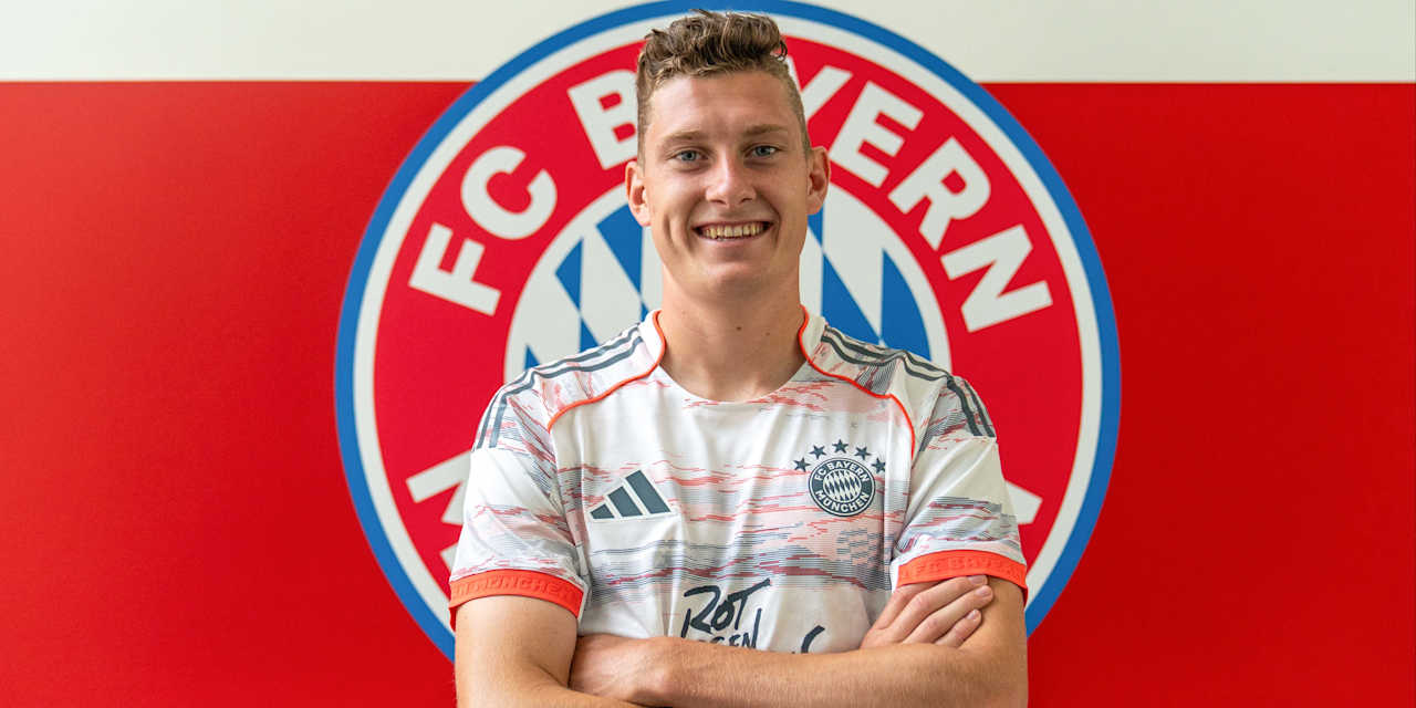 David Heindl und posiert im Trikot vor dem FC Bayern-Wappen am FC Bayern Campus.