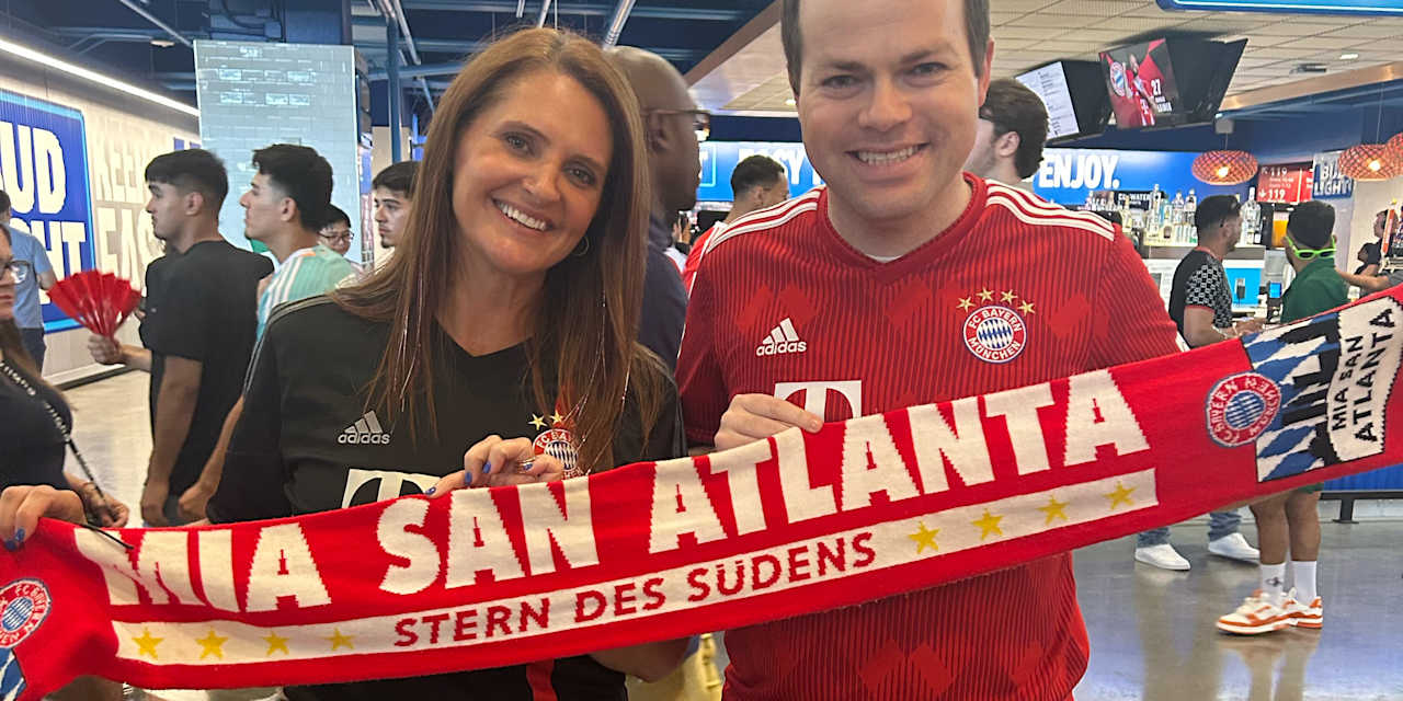 Heather Cooke and Chris Clute wearing Bayern jerseys and a Bayern scarf with the words ‘Mia san Atlanta’ written on it.