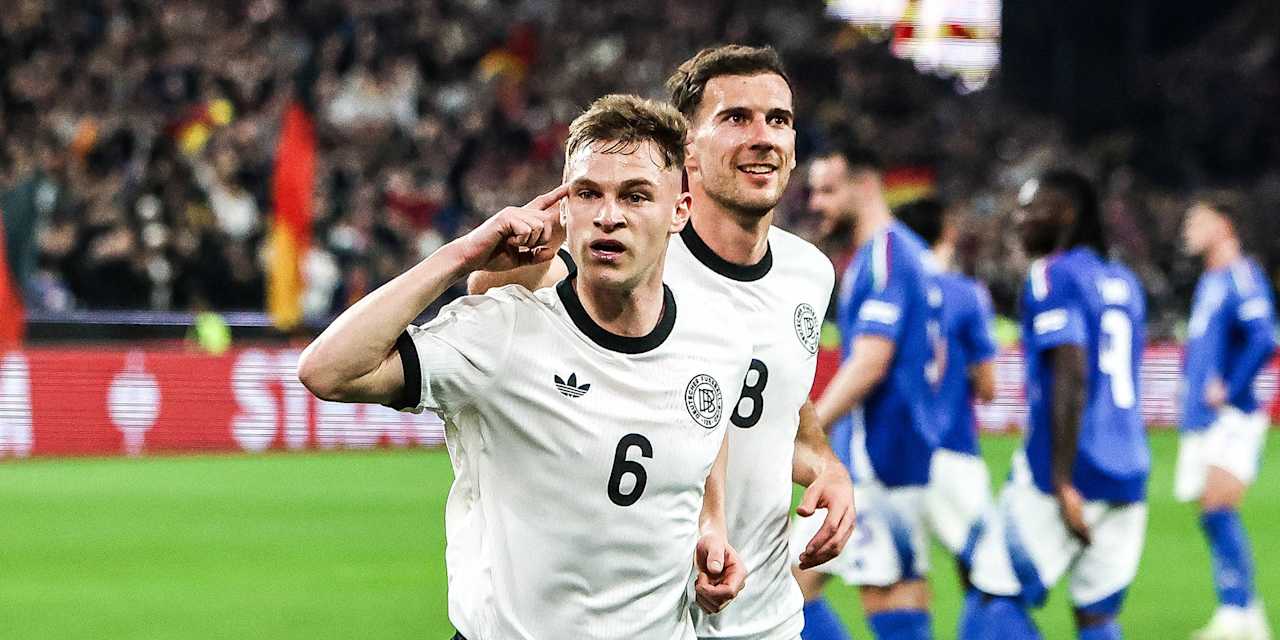 Joshua Kimmich jubelt im Trikot der deutschen Nationalmannschaft und zeigt mit dem Finger auf seine Stirn. Dahinter läuft Leon Goretzka.