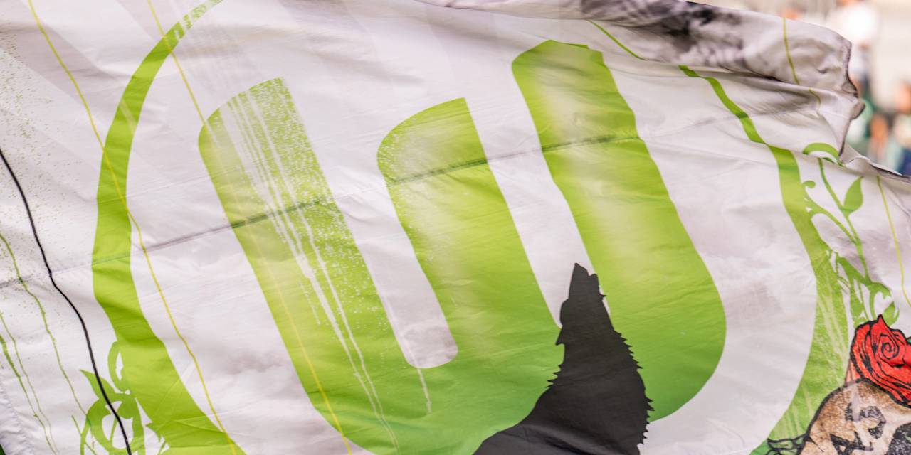 Eine Flagge mit dem Logo des VfL Wolfsburg. Im Vordergrund steht die Silhouette eines heulender Wolfs.