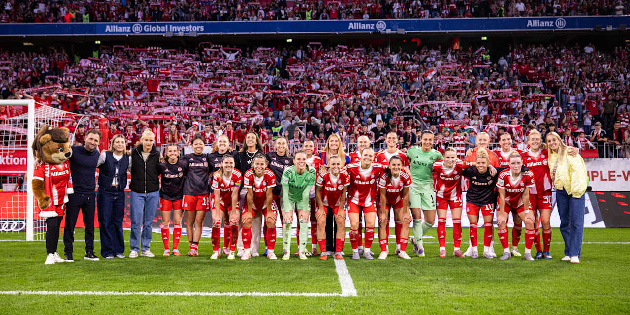 Die FC Bayern Frauen in einem Gruppenfoto vor der Südkurve der Allianz Arena mit Fans im Hintergrund.