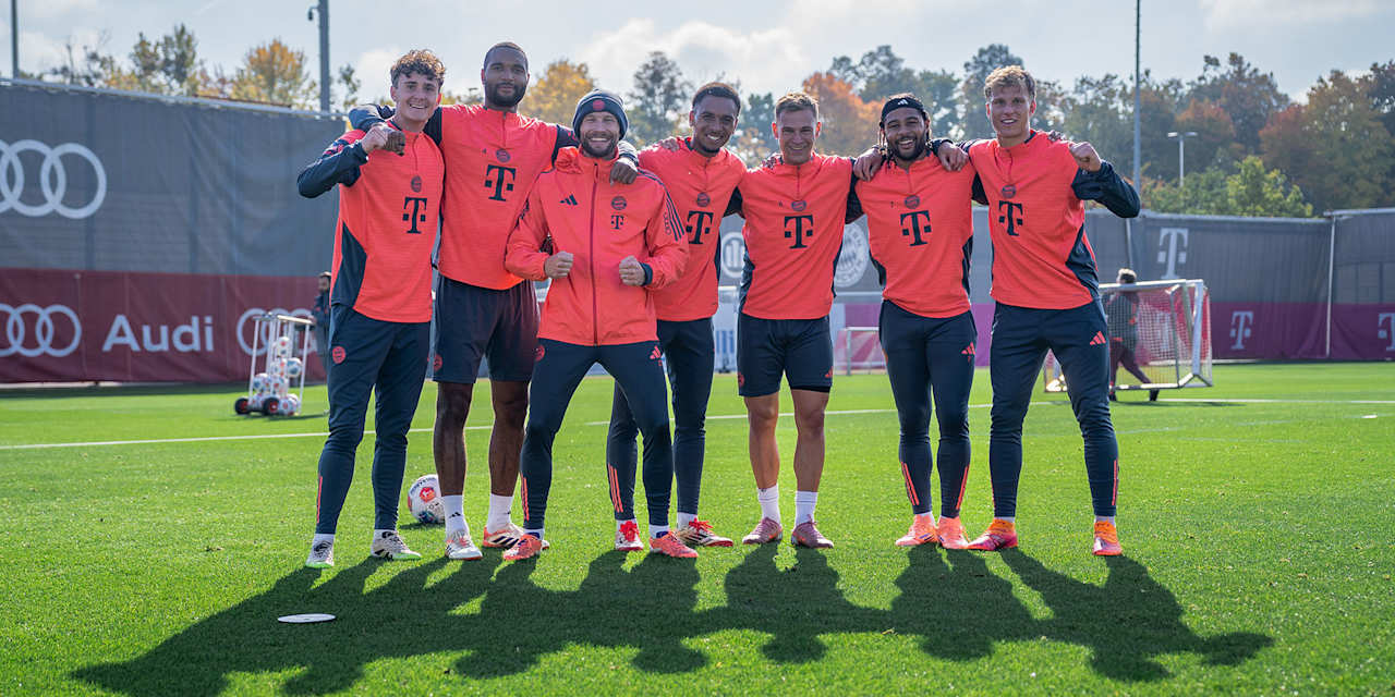 Die Bayern Spieler stehen Arm in Arm auf dem Trainingsplatz und grinsen in die Kamera.