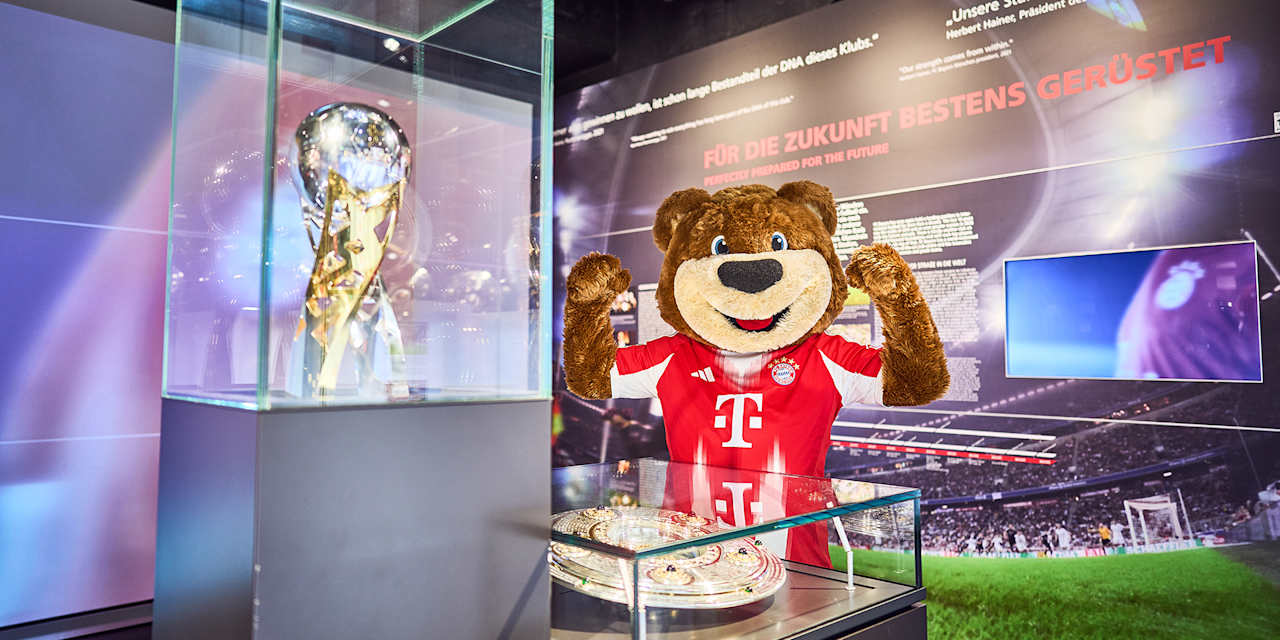 Maskottchen Berni posiert vor Pokalen im FC Bayern Museum