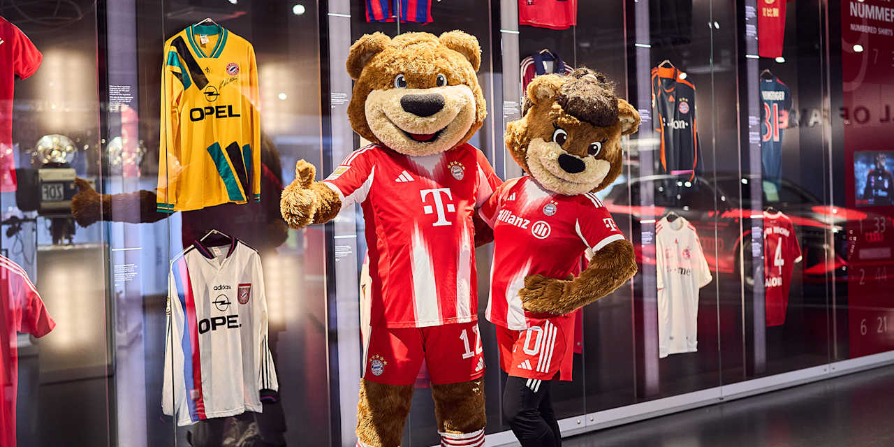 Die Maskottchen Berni und Mia posieren vor der Trikotwand im FC Bayern Museum