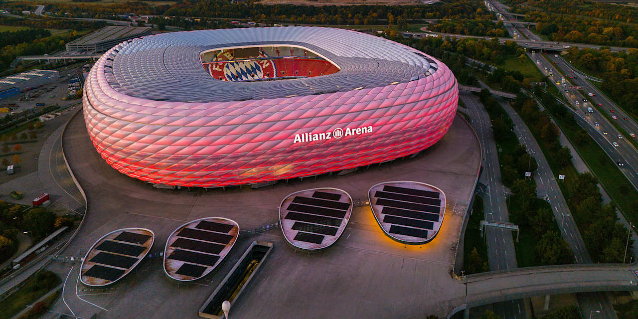Allianz Arena strahlt in der Dämmerung in Rot, daneben die Autobahn