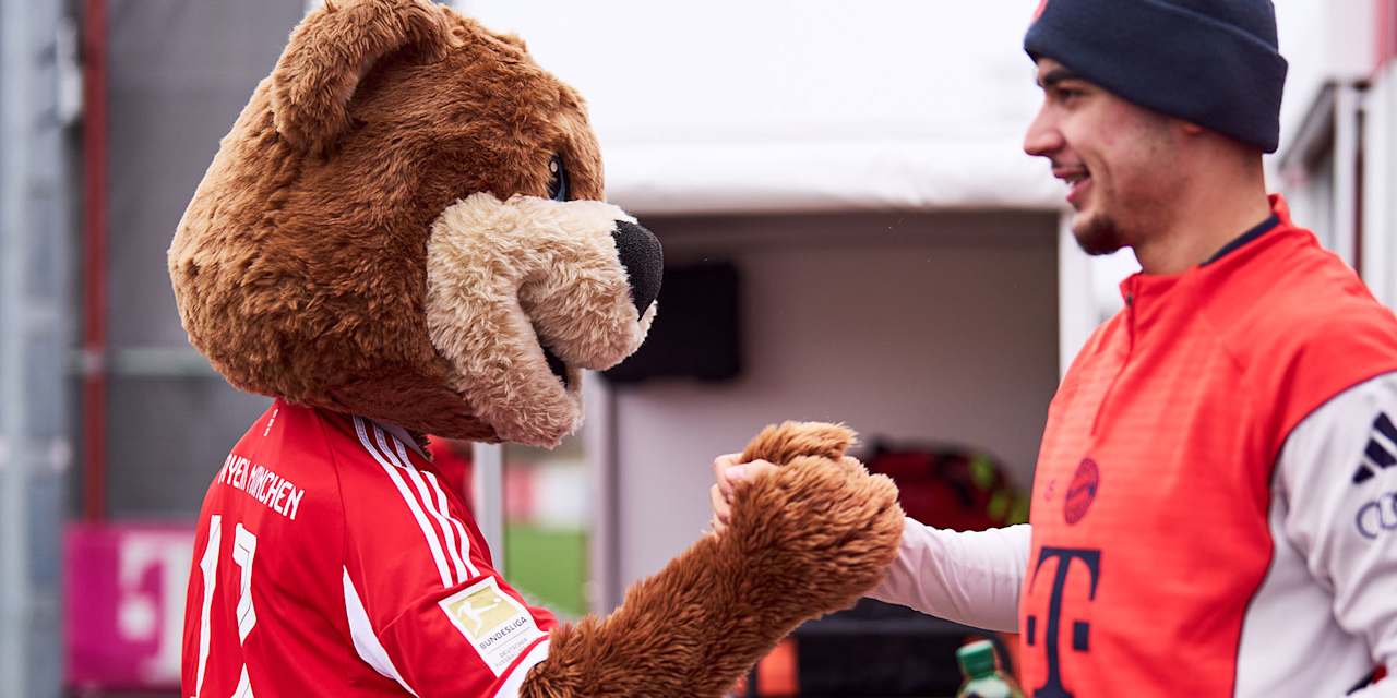 Maskottchen Berni und Aleksandar Pavlovic schlagen ein vor dem Training des FC Bayern