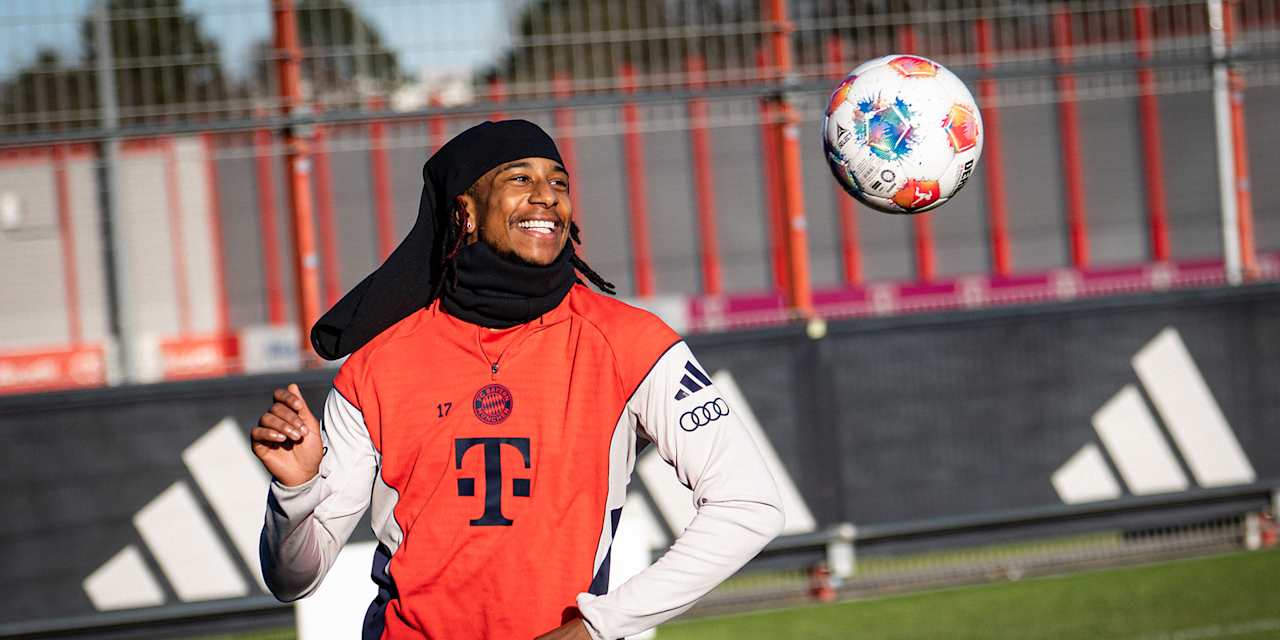 Michael Olise schaut einen Ball an und lacht im Training des FC Bayern