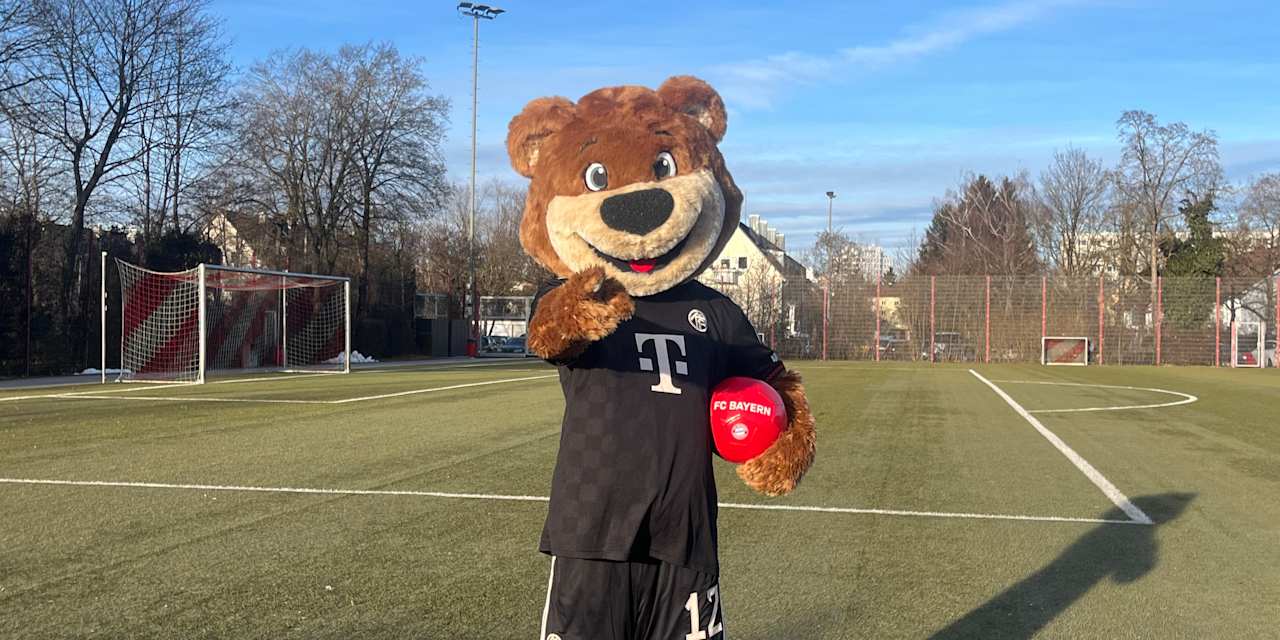 Berni steht auf dem Kunstrasenplatz mit einem Ball unterm Arm und zeigt in die Kamera.