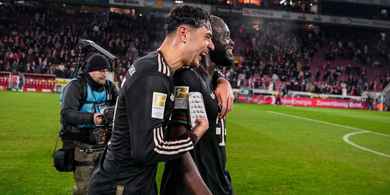Aleks Pavlovic umarmt lachend Dayot Upamecano nach dem Bundesliga-Sieg des FC Bayern beim 1. FC Köln